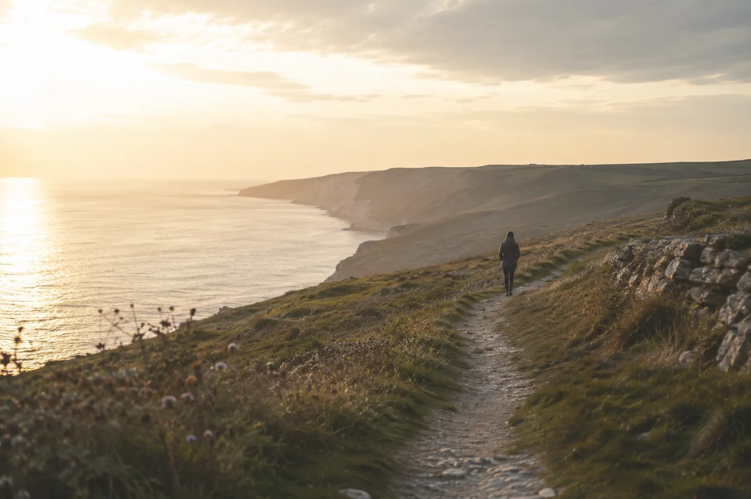 A person walking along a quiet coastal path at sunrise